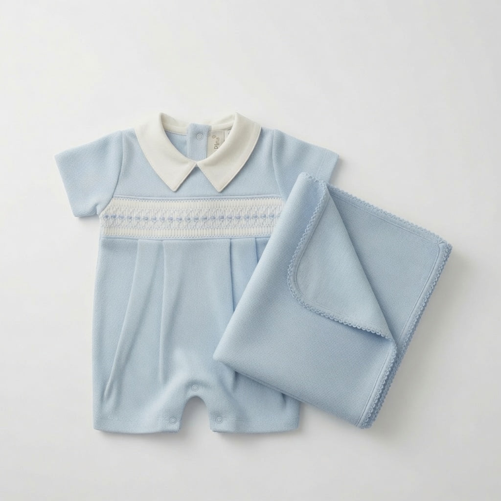 A baby short-sleeve romper in light blue with a white pointed collar and white hand-smocked trim across the chest, shown with a matching folded light blue blanket on a plain light background.
