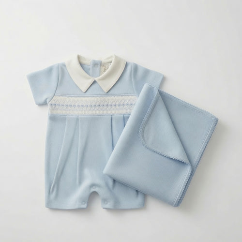 A baby short-sleeve romper in light blue with a white pointed collar and white hand-smocked trim across the chest, shown with a matching folded light blue blanket on a plain light background.