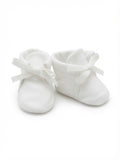 A pair of white soft fabric baby booties with matching ribbon bows, photographed on a seamless white background.