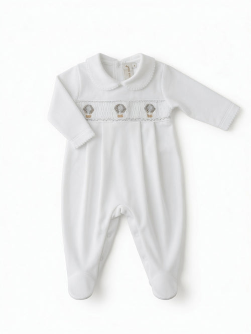 A white long-sleeve baby footie with a smocked chest panel featuring three small hot air balloon hand embroidery motifs, displayed flat against a white background from the front side.