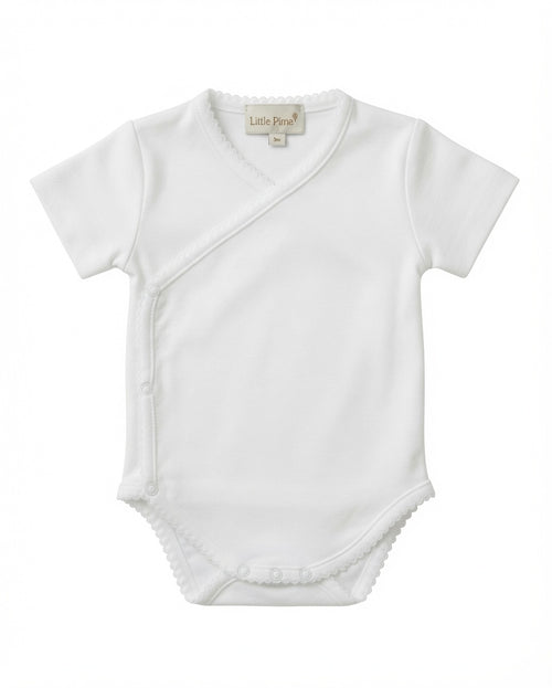 A white short-sleeve baby bodysuit with an asymmetrical wrap-style front and delicate scalloped edges, shown flat against a white background. The brand label 'Little Pima' is visible inside the collar.