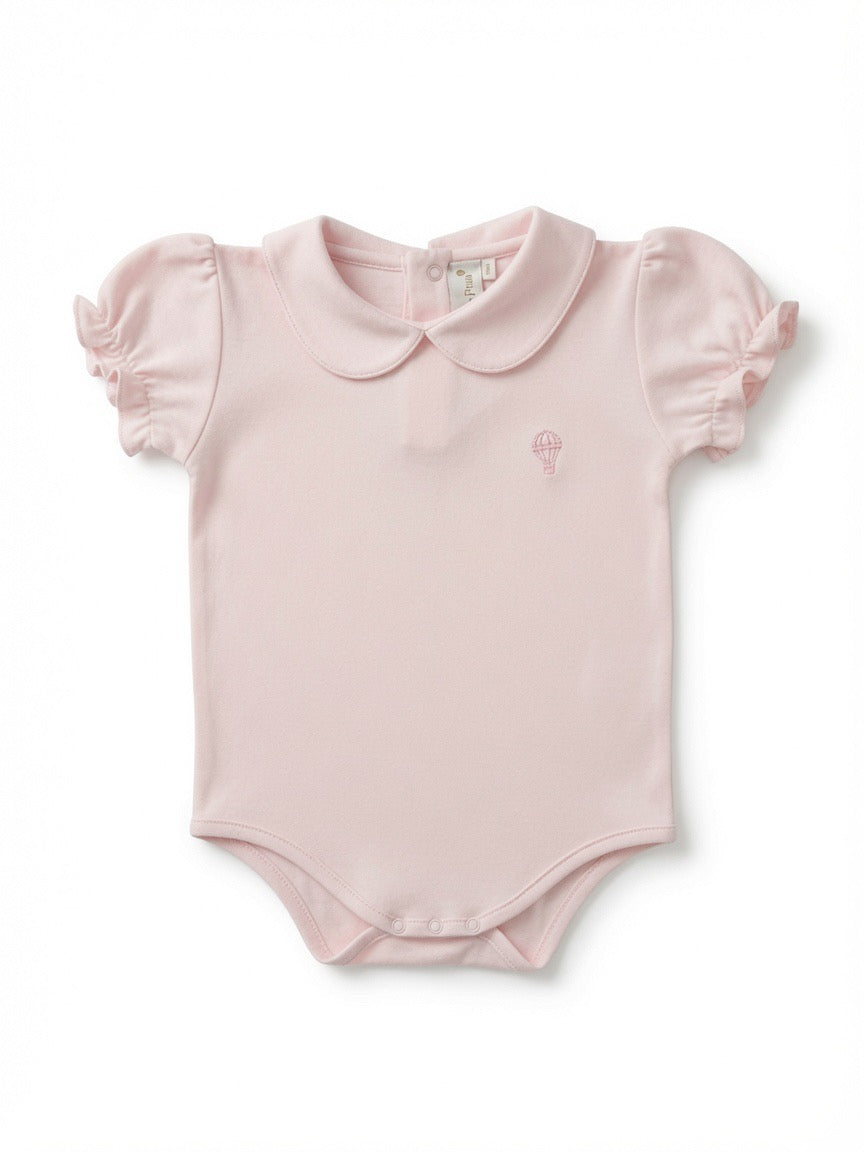 A light pink baby bodysuit with a Peter Pan collar, short ruffled sleeves, and a small embroidered hot air balloon logo on the left chest made from Peruvian Pima Cotton.